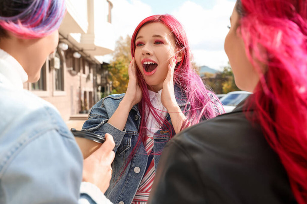 Surprised young woman with bright hair and her friends outdoors - Фото, изображение