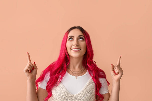 Beautiful woman with bright pink hair pointing at something on beige background - Fotografie, Obrázek