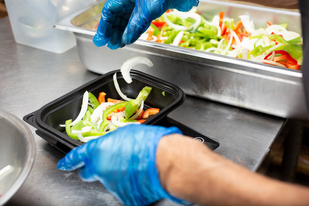 A view of a cook preparing vegetable ingredients into a meal prep container, in a restaurant kitchen setting. - Foto, Imagem