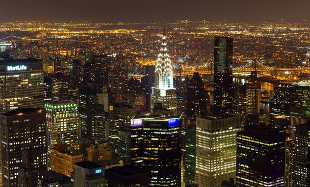 Нью-Йорк, штат Нью-Йорк, США - 28 декабря 2013 года: Высокий вид на Манхэттен до Квинса ночью. Здание Chrysler возвышается над другими зданиями в восточной части Манхэттена - Фото, изображение
