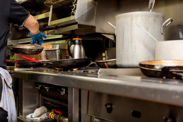 Ein niedriger Blickwinkel auf eine Restaurantküche mit Kochtöpfen, gegrilltem Essen, Unordnung und einem geschäftigen Koch. - Foto, Bild