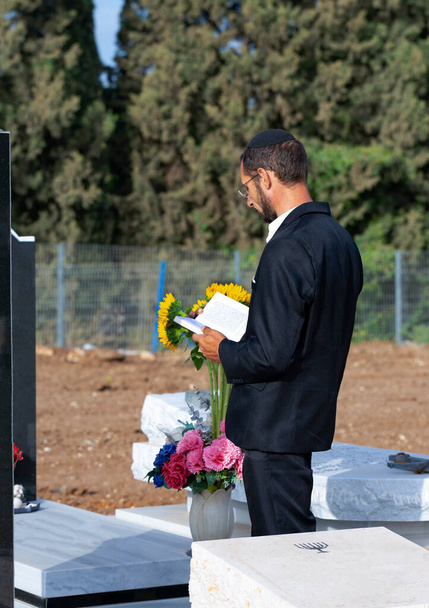 Siyah kippah içinde sakallı Yahudi 'nin İbranice İncil okuyup dua edişinin yan görüntüsü. İsrail 'de bir Yahudi mezarlığında dua etmek. Seçici odaklanma. Ormandaki eski Yahudi mezarlığı. Hasidik Yahudi Tevrat okuyor. - Fotoğraf, Görsel
