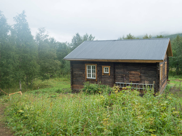 View of STF Njunjes Mountain cabin on a meadow, moody rainy day with thick fog. Wooden cottage lies on the banks of the Tarra river, at Padjelantaleden hiking trail. Lapland summer landscape - Foto, immagini
