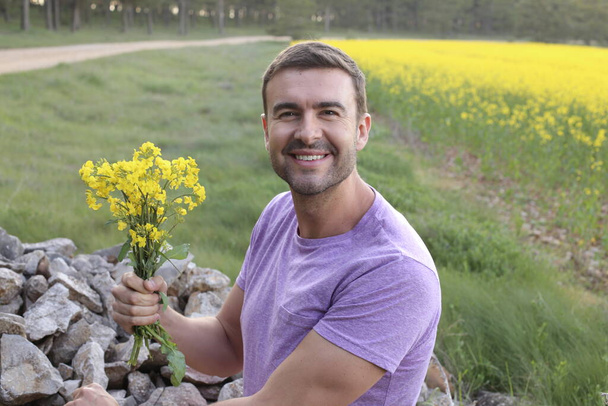 close-up portrait of handsome young man on beautiful yellow flowers meadow - 写真・画像