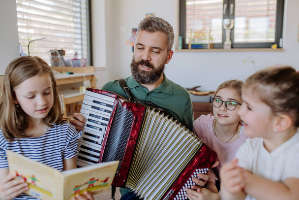 Cheerful father musician playing the accordion to his three little daughters at home. - Fotoğraf, Görsel