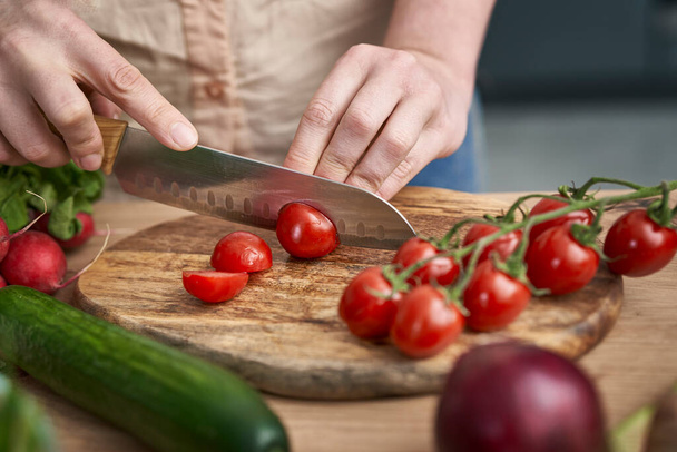 Woman cutting cherry tomatoes on wooden board - 写真・画像
