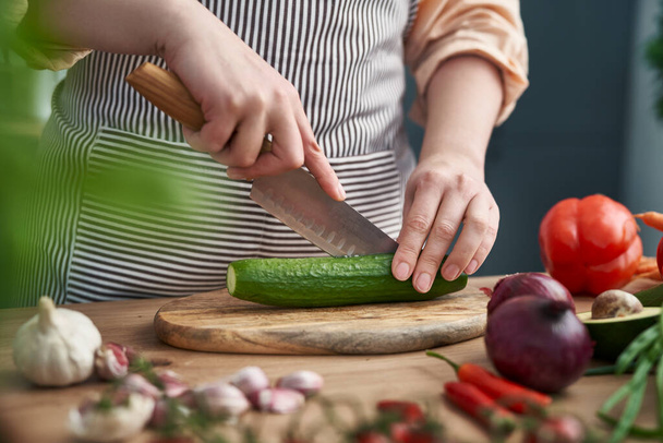 Close up of hands of woman cutting cucumber at the kitchen - Fotoğraf, Görsel