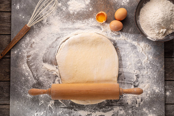 Ready to be baked dough. Top view of board, rolling pin and flour and dough. - Φωτογραφία, εικόνα
