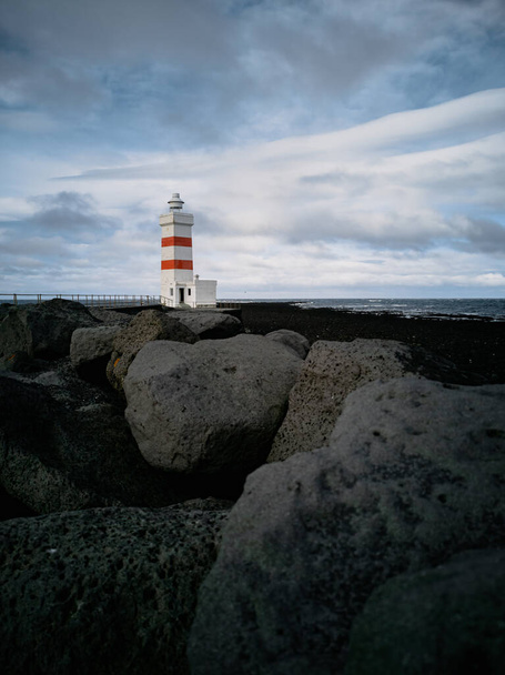 Lighthouse with red stripes wide angle over the black rocks - Zdjęcie, obraz