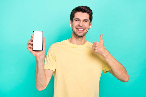 Photo of funny brunet young guy show telephone thumb up wear t-shirt headphones isolated on teal color background - Foto, Imagem