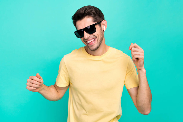 Photo of cute brunet millennial guy listen music dance wear eyewear t-shirt headphones isolated on teal color background - Foto, immagini