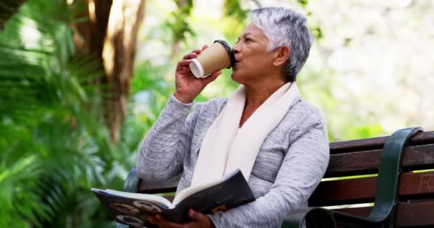Ottenere una bella lettura per oggi. 4k video di una donna matura che beve caffè mentre legge un libro nel parco. - Filmati, video