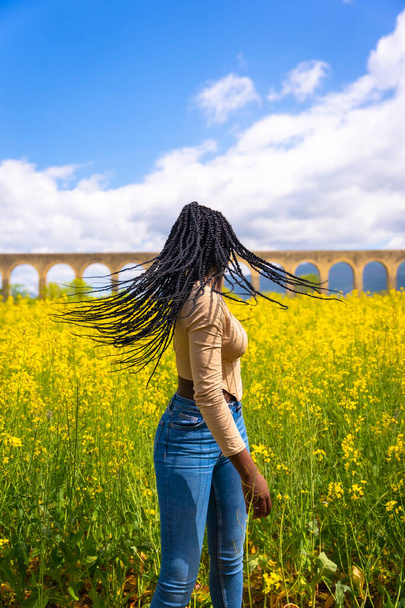 Estilo de vida pelo en movimiento, chica étnica negra con trenzas, viajero, en un campo de flores amarillas - Foto, Imagen