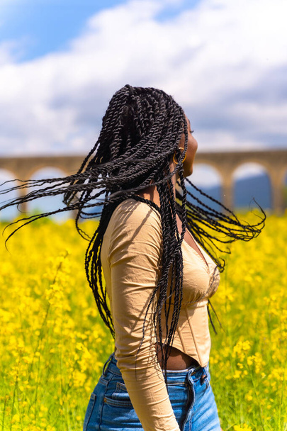 Lifestyle moving hair, portrait of black ethnic girl with braids, traveler, in a field of yellow flowers - Foto, Imagem