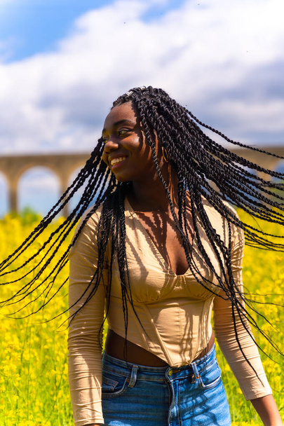 Lifestyle moving hair, portrait of black ethnic girl with braids, traveler, in a field of yellow flowers - Zdjęcie, obraz