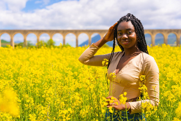 Lifestyle, portrait of a black ethnic girl with braids looking at camera, trap music dancer, in a field of yellow flowers - Foto, imagen