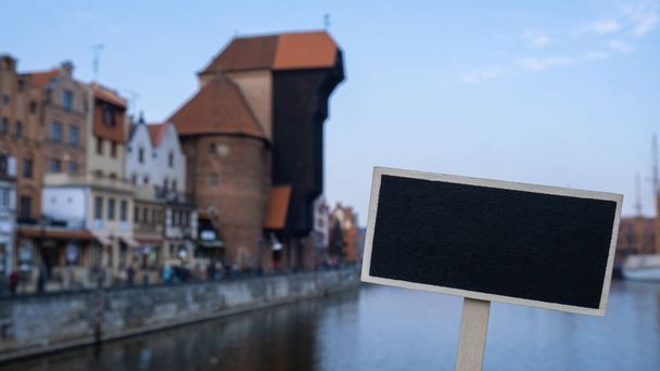 Empty mockup template Blackboard label against Gdansk beautiful old town over Motlawa river. The Zuraw Crane and colorful gothic facades of the old town in Gdansk, Poland. Visit Gdansk historical capital of Polish Pomerania with beautiful architectur - Foto, Imagem