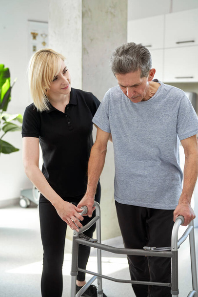 Senior man using a walker with the assistance of a nurse  - Foto, afbeelding