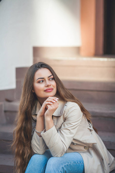 Portrait of a young beautiful long-haired woman in a European city. A model in stylish casual wear is relaxing outside. Spring. - Valokuva, kuva