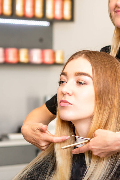 Beautiful young blonde woman with long straight blonde hair getting a haircut at the hairdresser salon - Zdjęcie, obraz