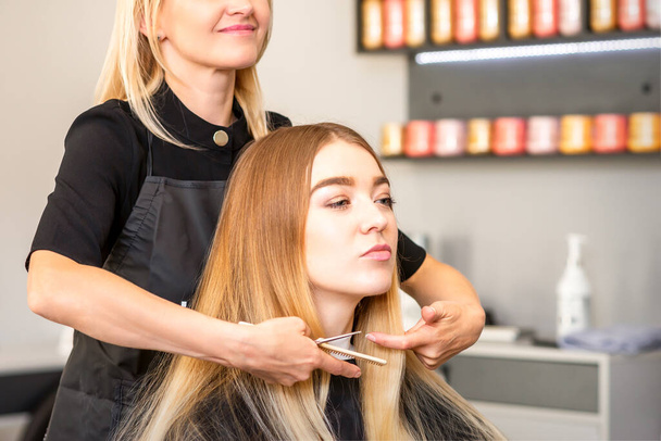 Beautiful young blonde woman with long straight blonde hair getting a haircut at the hairdresser salon - Photo, Image