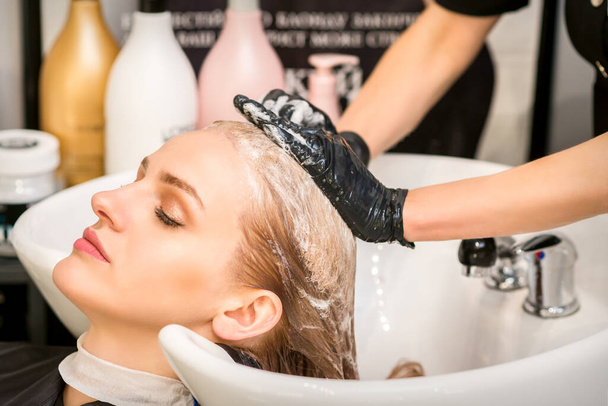 Young caucasian woman with closed eyes getting washing hair by a professional hairdresser in a beauty hair salon - Photo, Image
