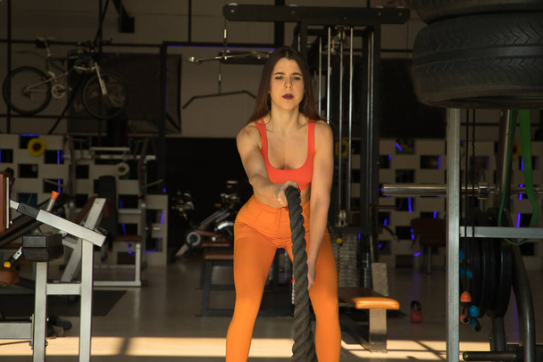 Young beautiful woman performing arm exercises with thick ropes in a gym. Fitness concept, weights, bodybuilding, gymnastics, muscles. - Photo, Image