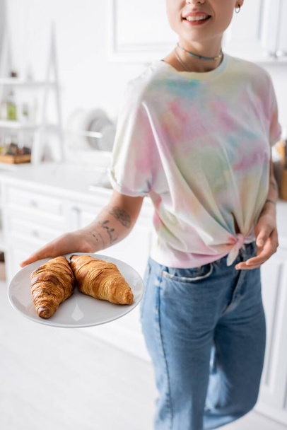 kivágott kilátás mosolygós nő gazdaság lemez ízletes croissant a konyhában - Fotó, kép