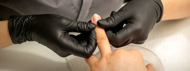 Close-up professionele manicure meester houdt de vrouwelijke hand van de klant en controleert de manicure in een nagel salon - Foto, afbeelding