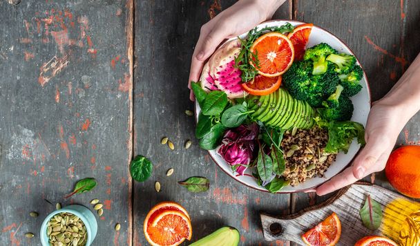 Girls' hands holding Quinoa vegetable vegetarian buddha bowl avocado, blood orange, broccoli, watermelon radish, spinach, quinoa, pumpkin seeds. top view. - Photo, Image