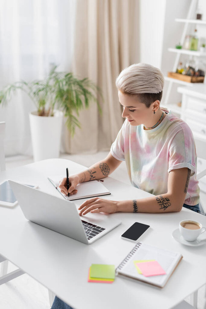 stylish woman writing in notebook near gadgets and coffee cup on kitchen table - Foto, immagini