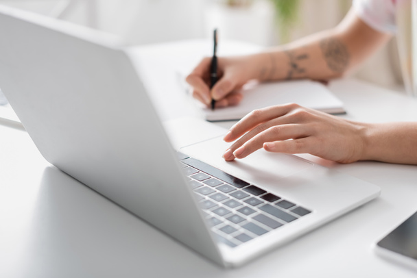częściowy widok kobiety piszącej w niewyraźnym notebooku przy laptopie  - Zdjęcie, obraz