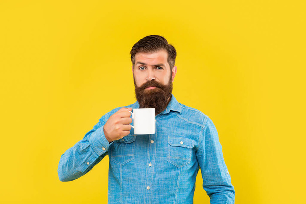 Winking guy holding tea mug yellow background - Zdjęcie, obraz
