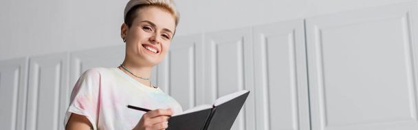 low angle view of happy woman with trendy hairstyle writing in notebook, banner - Foto, immagini