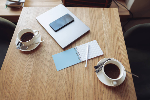 Shora na stole v kavárně s kávou ve dvou šálcích, notebooku, smartphonu a notebooku s perem. - Fotografie, Obrázek
