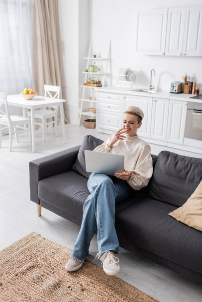 high angle view of woman in jeans sitting with laptop on sofa in open plan kitchen - Valokuva, kuva