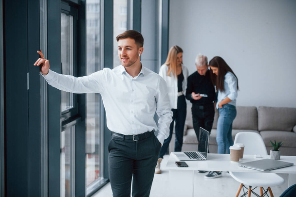 Man in formal clothes standing in front of young successful team that working and communicating together indoors in office. - 写真・画像