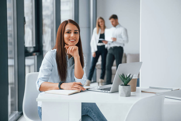 Woman with laptop sitting in front of group of young successful team that working and communicating together indoors in office. - Фото, зображення