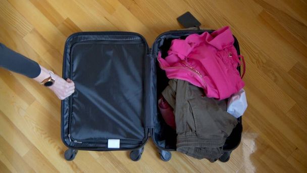 An open suitcase lies on the floor, things for the trip are casually thrown into it. - Foto, afbeelding
