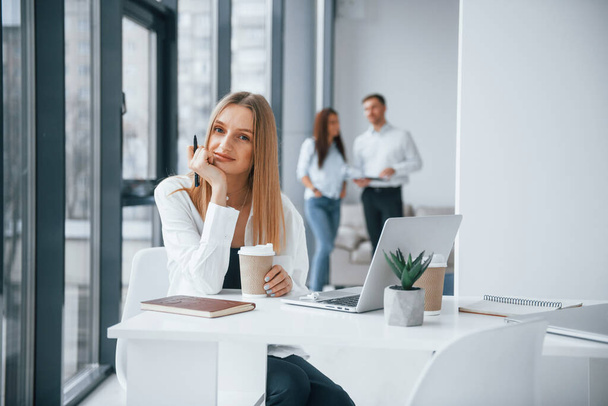 Woman with laptop sitting in front of group of young successful team that working and communicating together indoors in office. - Photo, image
