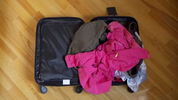 Avoin matkalaukku on lattialla, matkatavarat heitetään siihen satunnaisesti.. - Valokuva, kuva