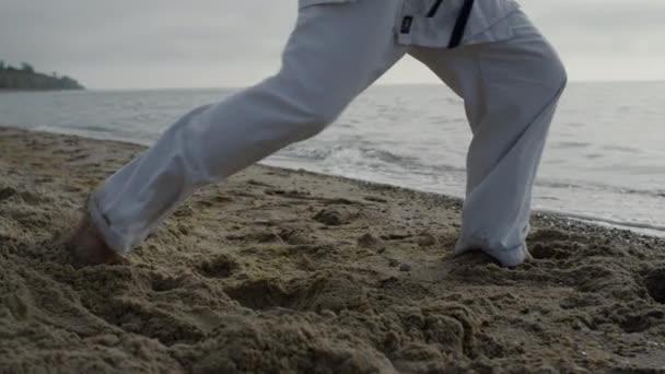 Neznámé mužské nohy dělají karate kopy do písku zblízka. Sportovec šlape na pláž - Záběry, video