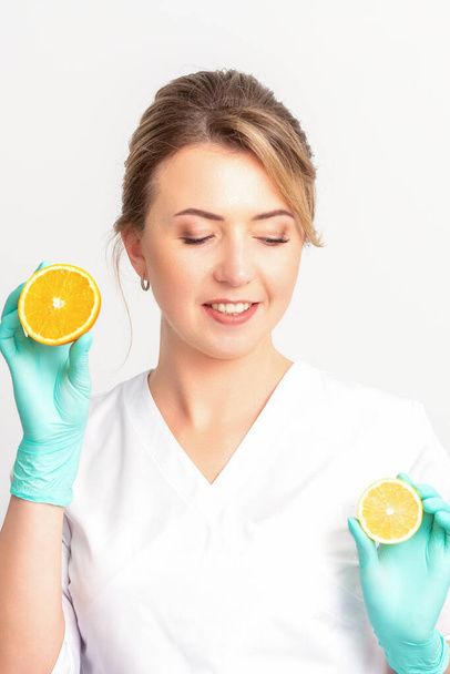 Smiling female nutritionist holding a sliced orange, looking at camera over white background, healthy diet concept - Zdjęcie, obraz