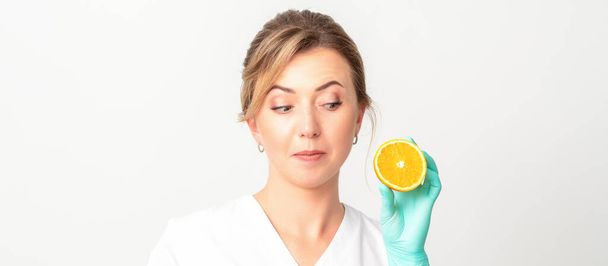 Smiling female nutritionist holding a sliced orange, looking at camera over white background, healthy diet concept - Foto, Bild