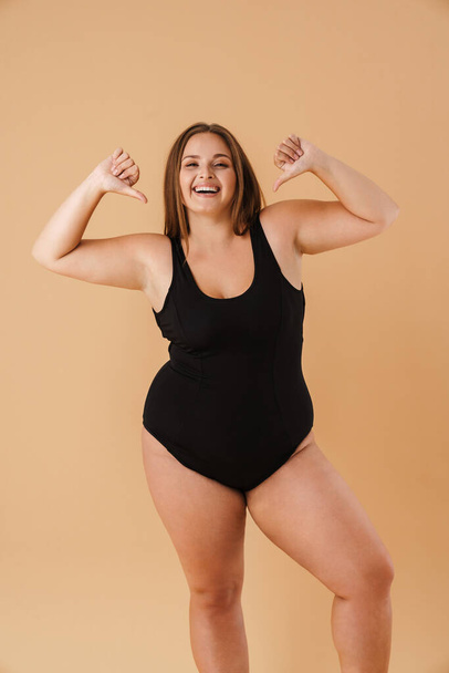 Young woman wearing swimsuit smiling and pointing fingers at herself isolated over beige wall - Foto, imagen