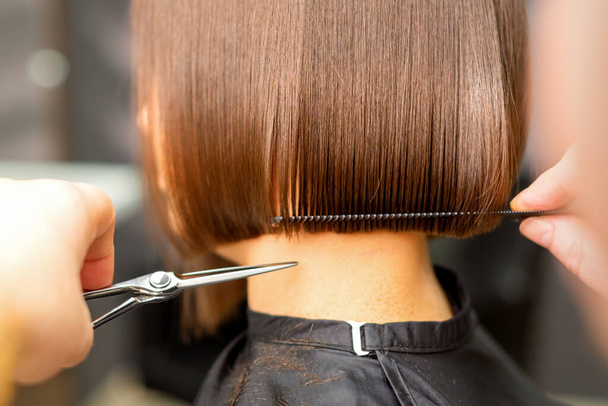 Coupe de cheveux courts de jeune femme blanche par les mains d'un coiffeur dans un salon de coiffure, vue de dos, gros plan - Photo, image