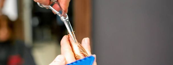 Стрижка кінчиків рудого волосся з гребінцем і ножицями руками чоловіка-перукаря в перукарні, крупним планом
 - Фото, зображення