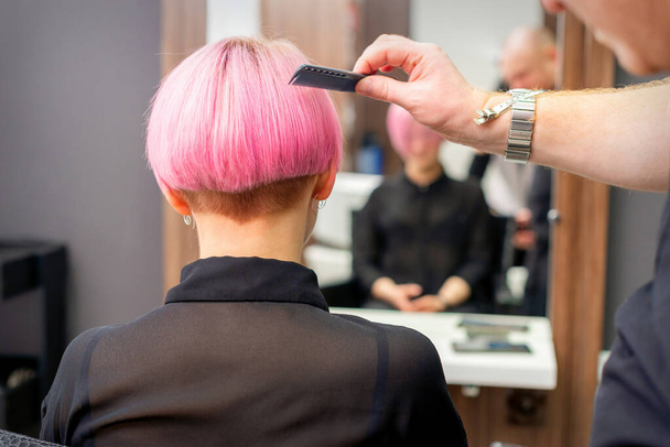Ein Friseur kämmt die rosa gefärbten kurzen Haare der Kundin im Friseursalon, Rückseite - Foto, Bild