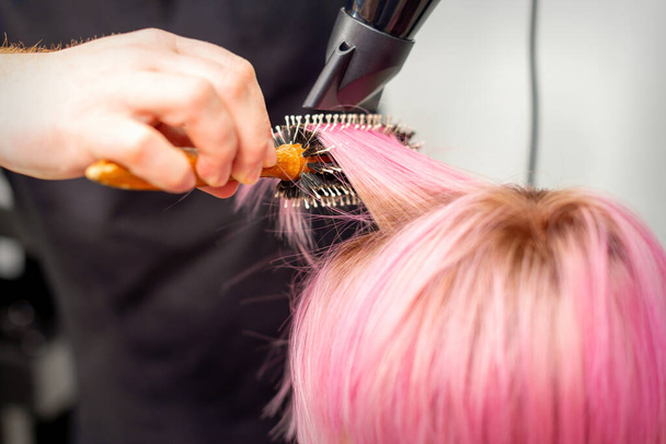 若い白人女性の短いピンクの髪を乾燥黒髪と黒丸みを帯びたブラシで髪サロンの男性の美容師の手で、クローズアップ - 写真・画像