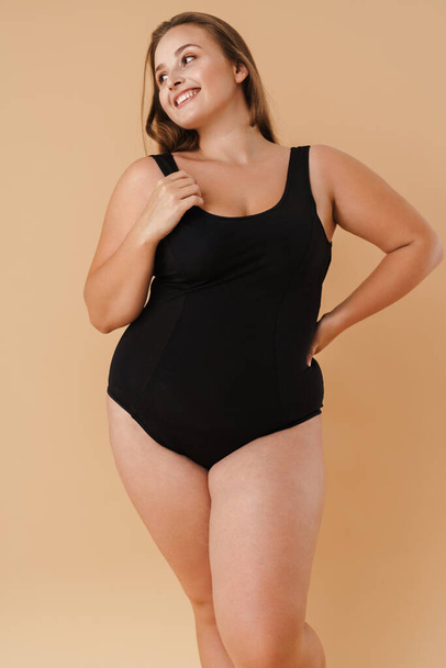 Young woman wearing swimsuit smiling and looking aside isolated over beige background - Photo, image